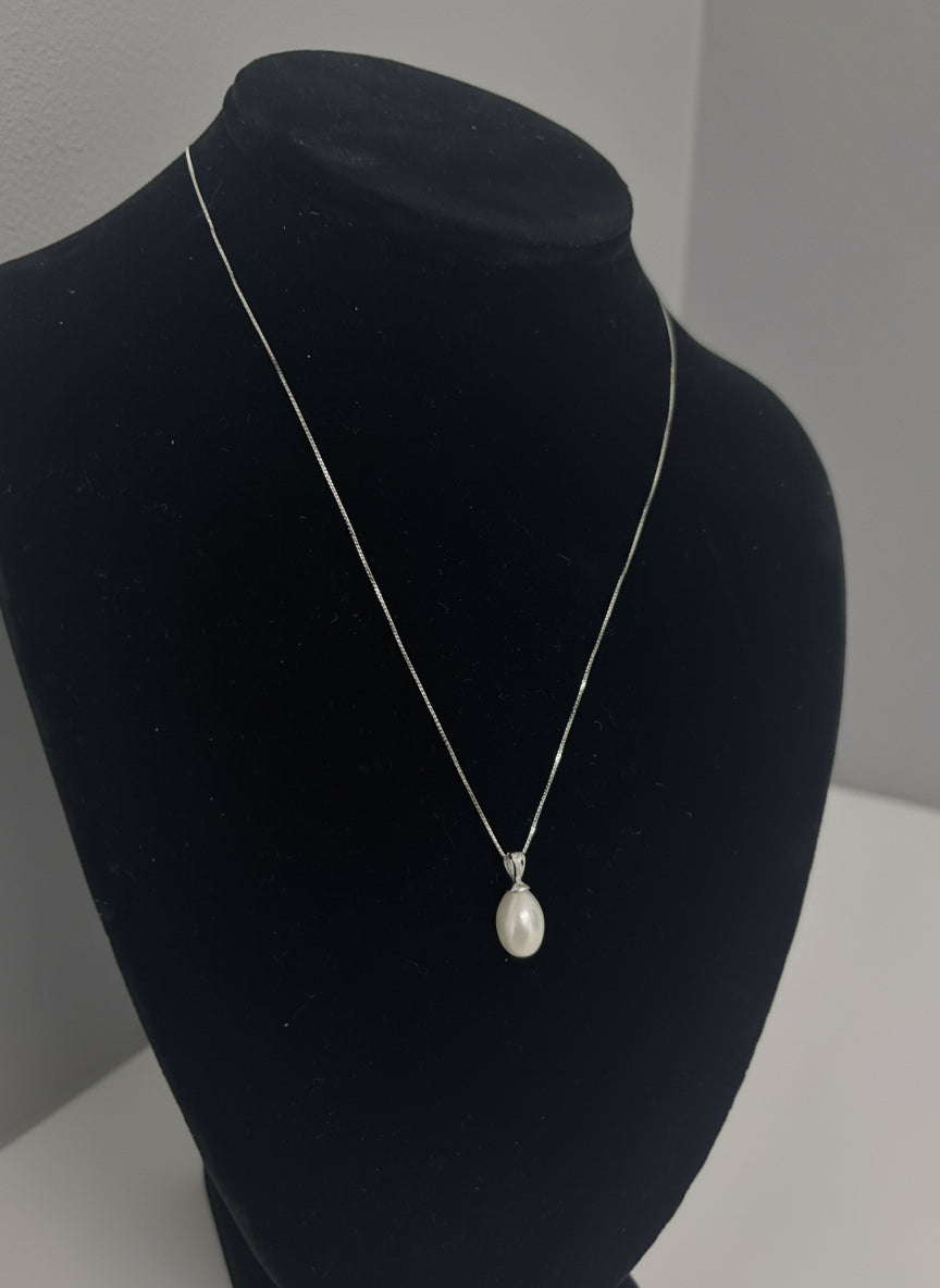 Pearl pendant on a black mannequin head against a plain background