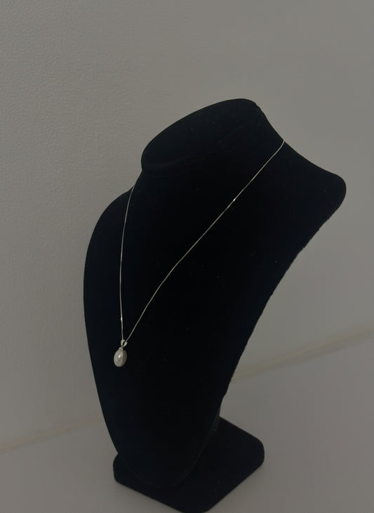 Pearl pendant on a black mannequin head against a plain background, side angle