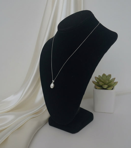 Pearl pendant on a black mannequin head against a plain background, side angle