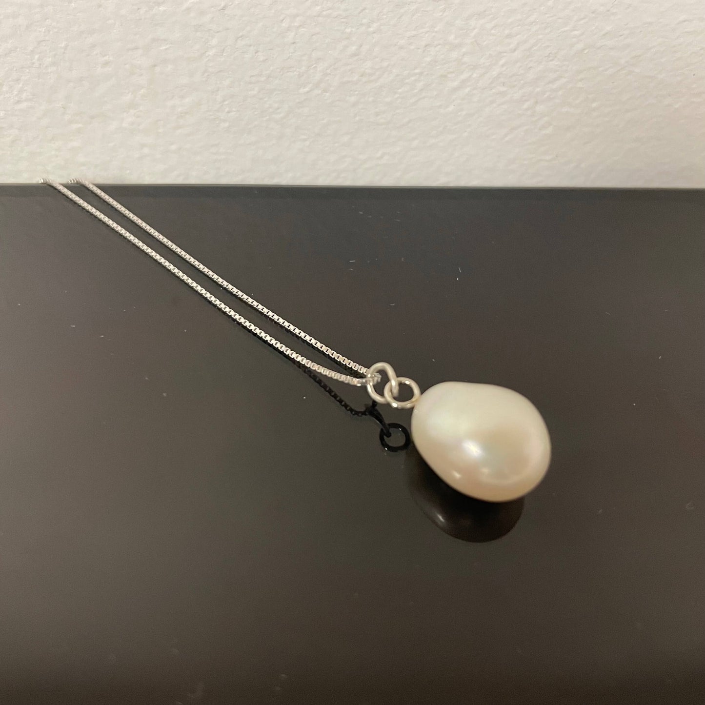 Pearl necklace on a black surface with a white background