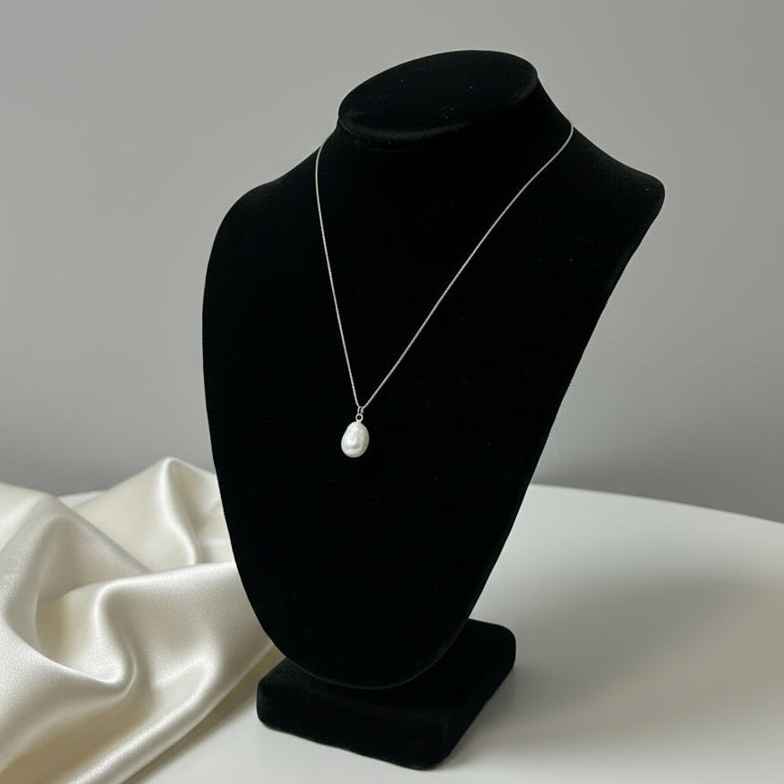 Pearl necklace on a black velvet stand against a white background