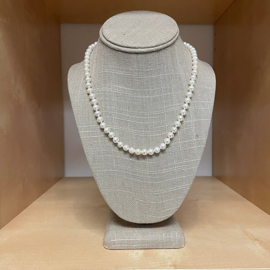 Pearl necklace on a gray fabric bust against a wooden background