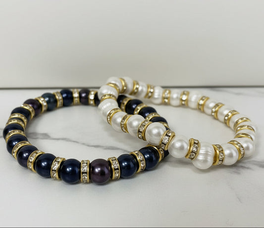Two beaded bracelets with black, gold, and pearl beads on a beige surface.